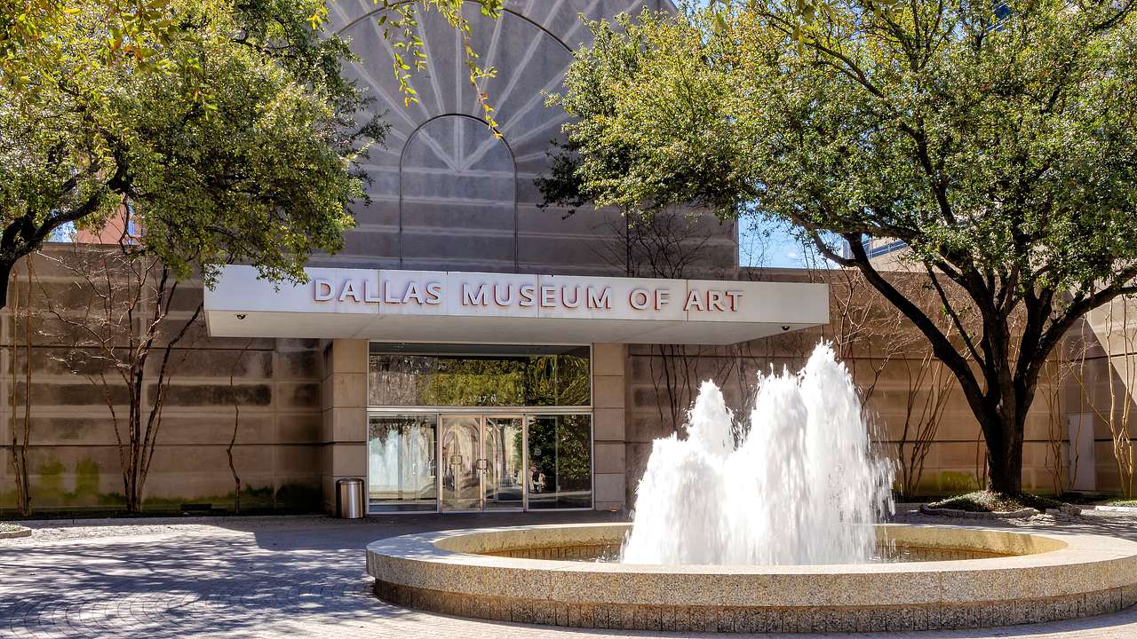 A building with a sign saying "Dallas Museum of Art" and a circular fountain in front