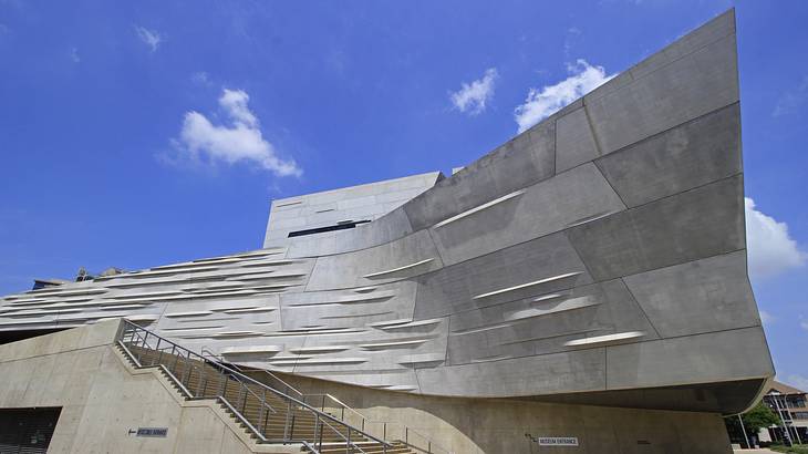 A gray contemporary-style building with stairs next to a blue sky with clouds