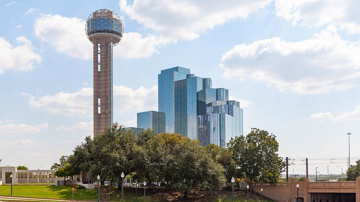 A tower with a sphere-shaped top and a modern skyscraper next to grass and trees