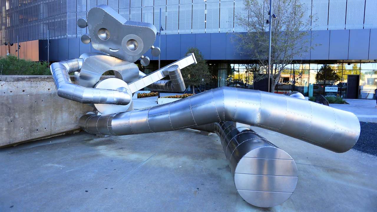 A stainless steel sculpture of a robot sitting down with a banjo