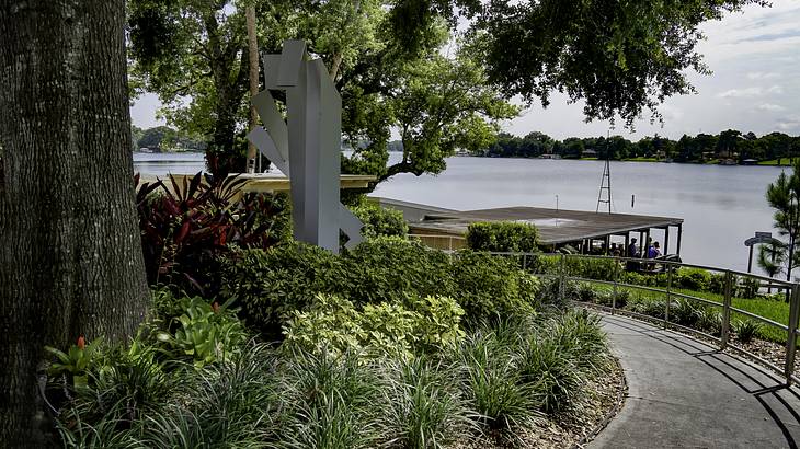 A path walk surrounded by a garden with plants and trees that overlooks a lake