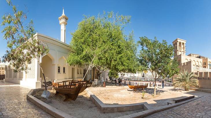 A square with trees and old stone Islamic-style buildings on a clear day