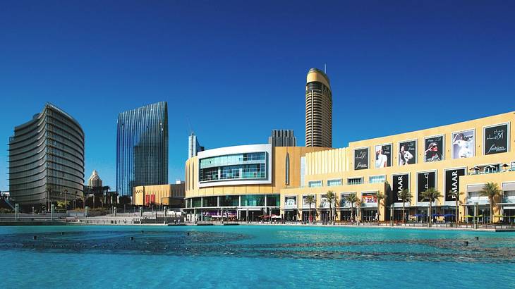 A shopping mall and tall buildings next to a pool of water under a blue sky