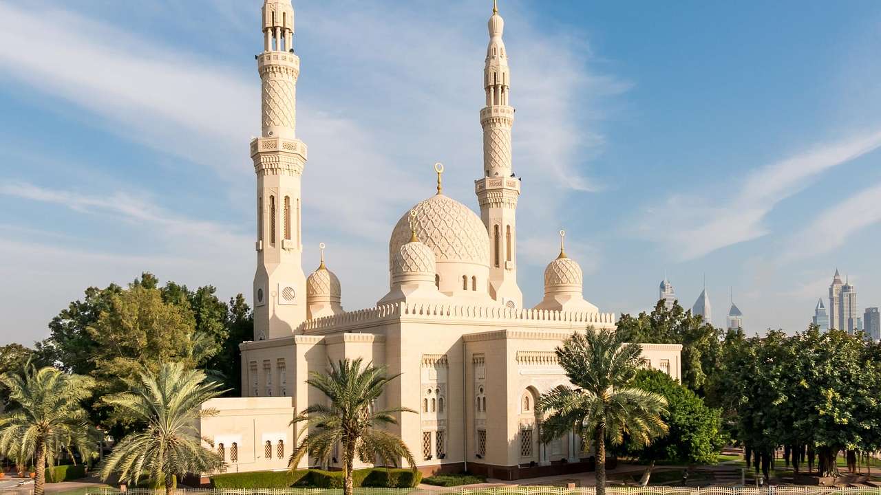 An Islamic mosque with domes and towers next to palm trees