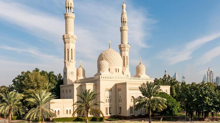 An Islamic mosque with domes and towers next to palm trees