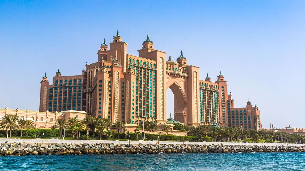The regal Atlantis Hotel with an arch and towers next to trees and the water