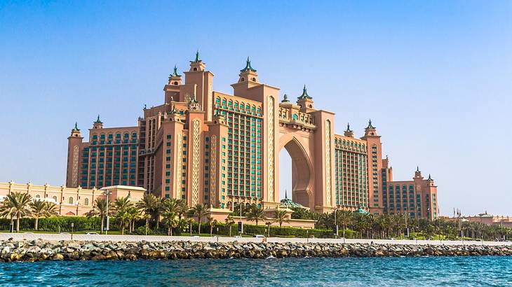 The regal Atlantis Hotel with an arch and towers next to trees and the water