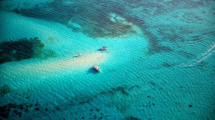 Aerial shot of the sea with boats by a sandbar