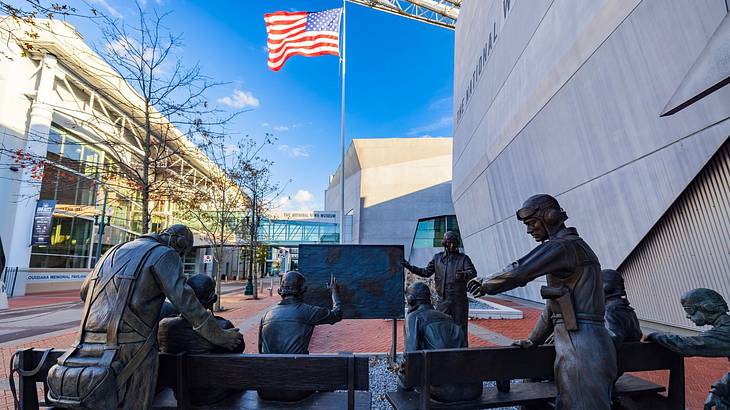 Human statues, some sitting and some standing, with the United States flag in front