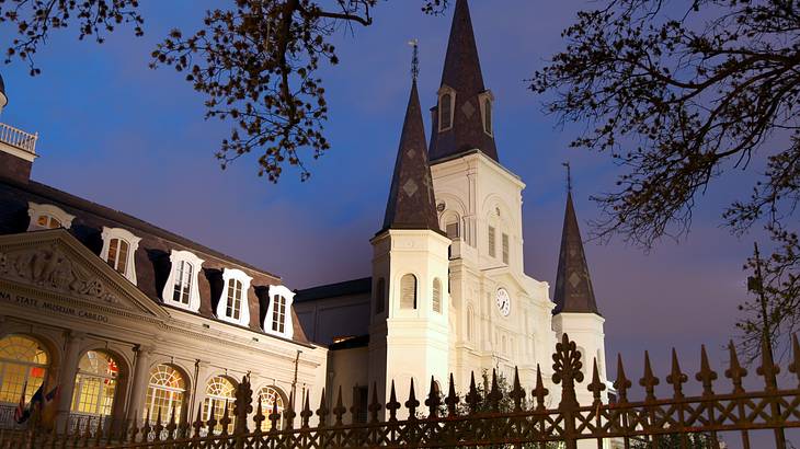 A white cathedral with black spires behind an iron fence at night
