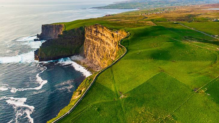 Cliffs with green pasture being lapped by waves below