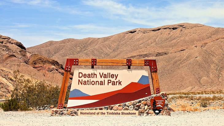 A concrete sign saying "Death Valley National Park" with mountains in the background