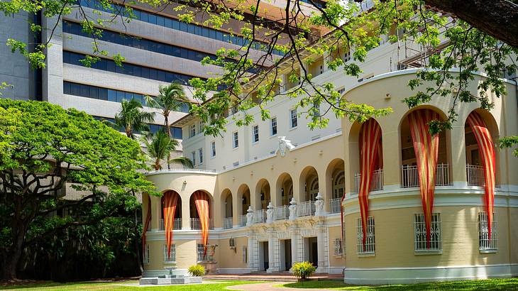 A building with arches and orange drapes in a garden with a taller building behind