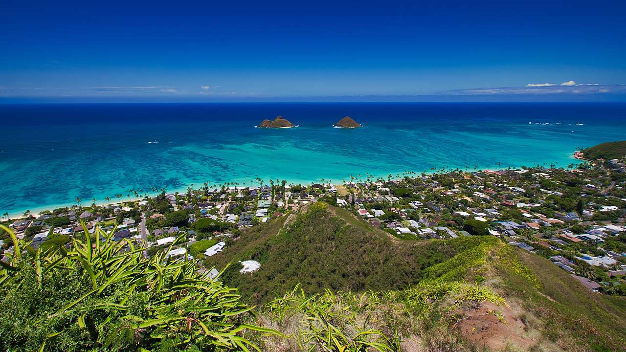 A grassy ridge overlooking a town with a view of turquoise waters and small islands