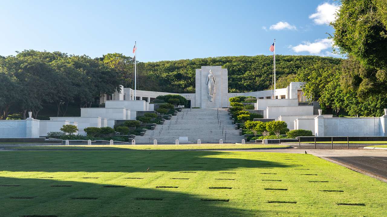Rows of graves with a monument that has two flags on each side, surrounded by trees