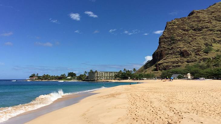 A sandy beach next to the ocean and a cliff under a blue sky