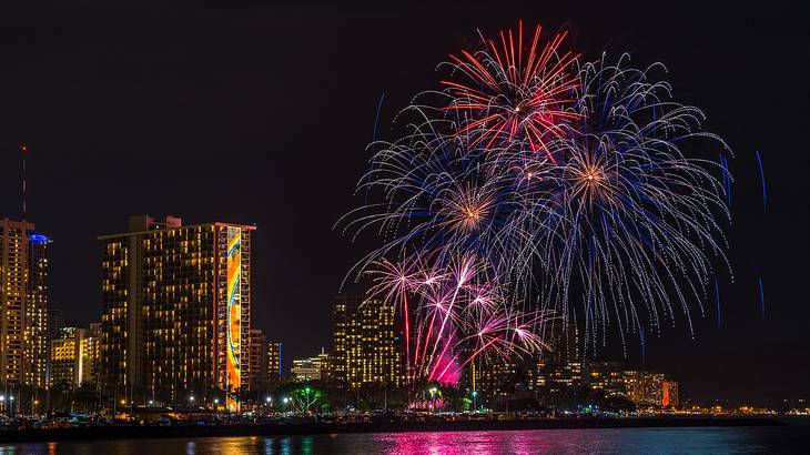 Colorful fireworks next to buildings and the ocean at night