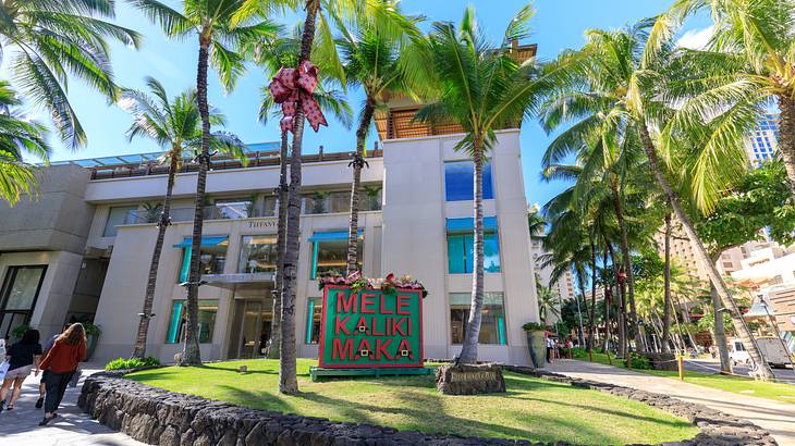 A white building with palm trees and a sign in front