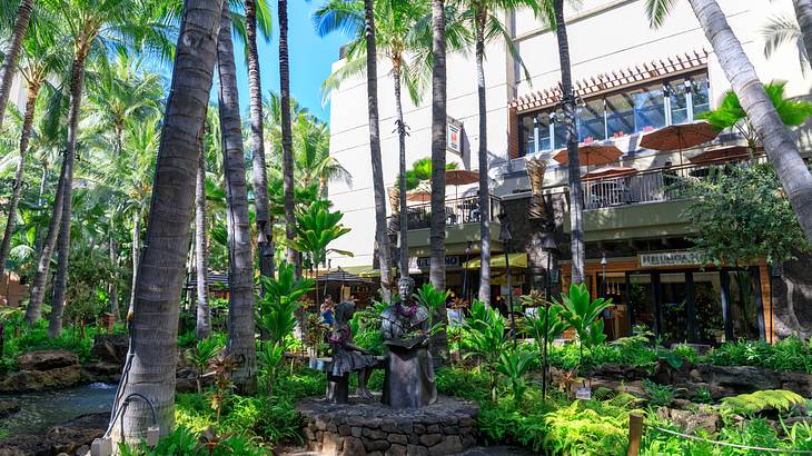 A building with lots of palm trees, greenery, and statues in front of it