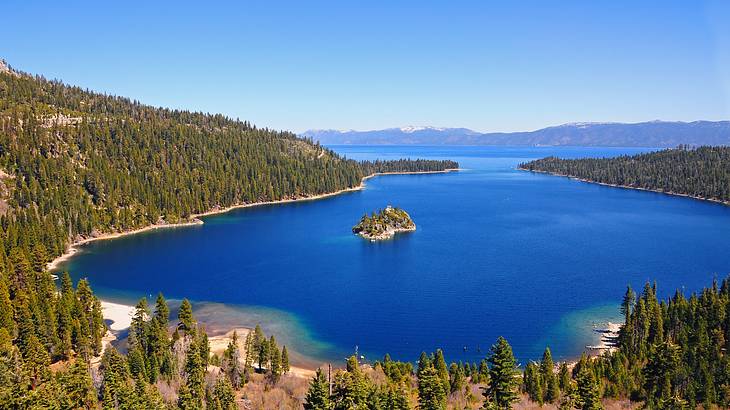 Aerial shot of a lake with an islet in the middle near forested mountains