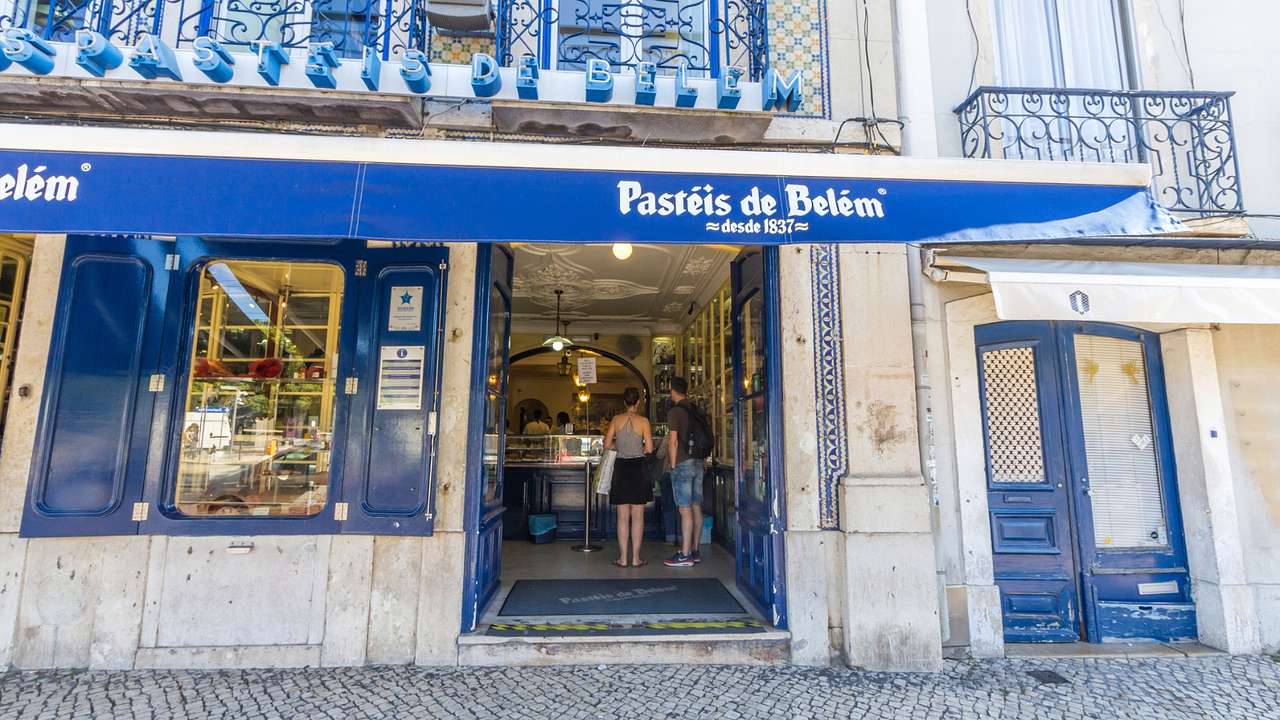 The exterior of a Portuguese bakery with a blue sign that says "Pastéis de Belém"