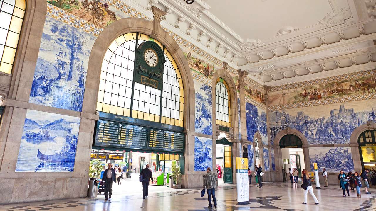 The interior of a train station with a clock and blue and white murals on the walls