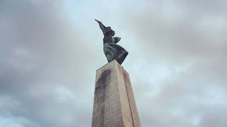 A statue on top of a tall stone pedestal next to a cloudy and overcast sky