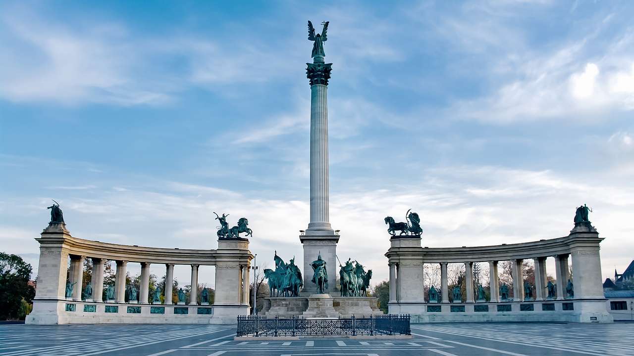 A square with an obelisk at the center surrounded by statues and two columned walls