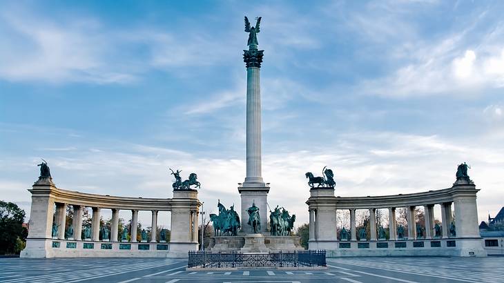 A square with an obelisk at the center surrounded by statues and two columned walls