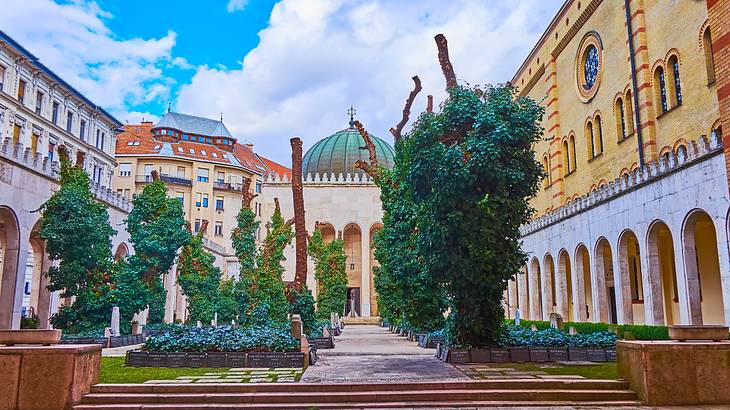 A courtyard with a central path, trees and plants, and a domed building in the back