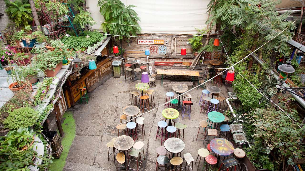 A space with colorful mismatched tables and stools, surrounded by plants