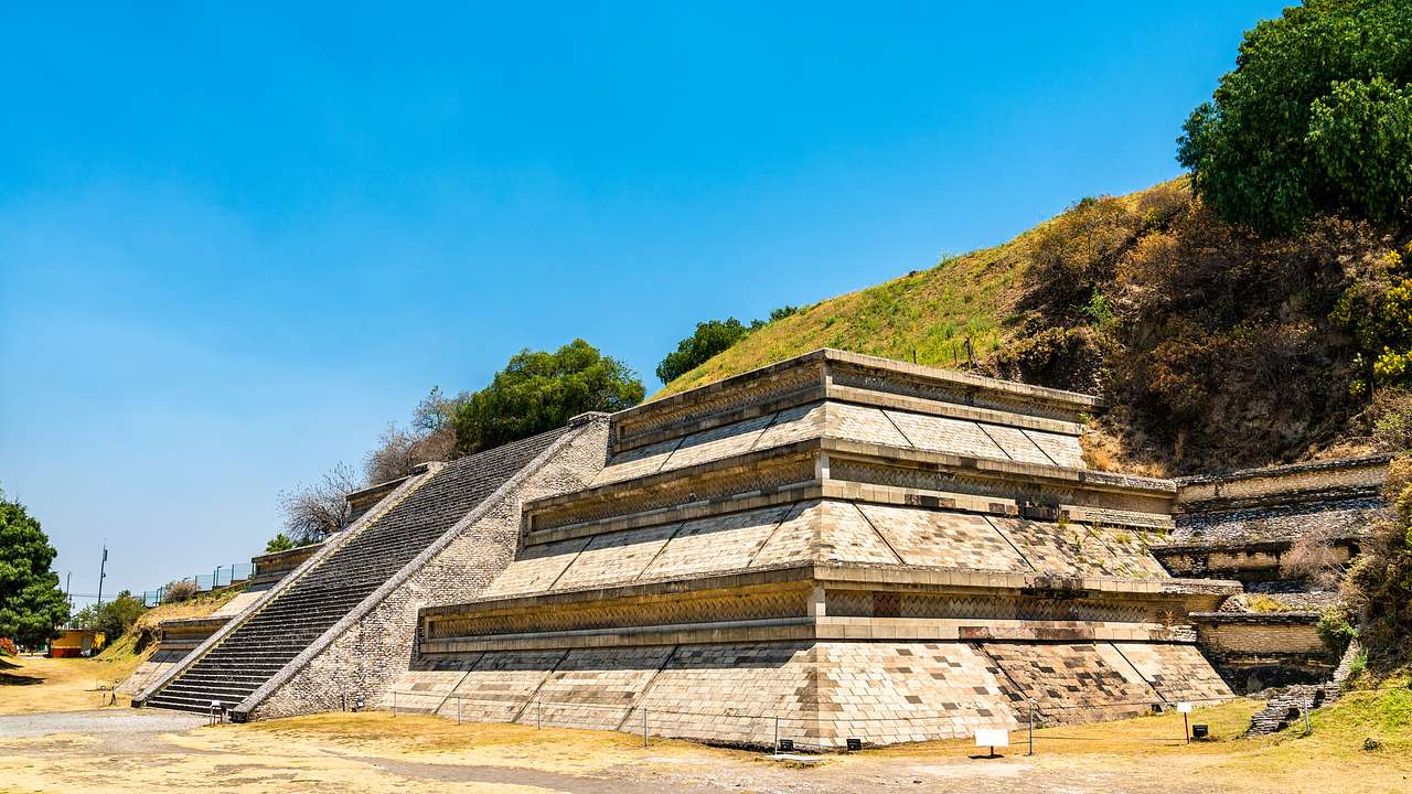 A hill and trees against an old, stone pyramid with steps