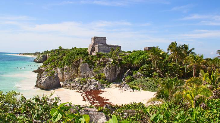 Old Mayan ruins atop a rocky cliff surrounded by greenery overlooking the blue water