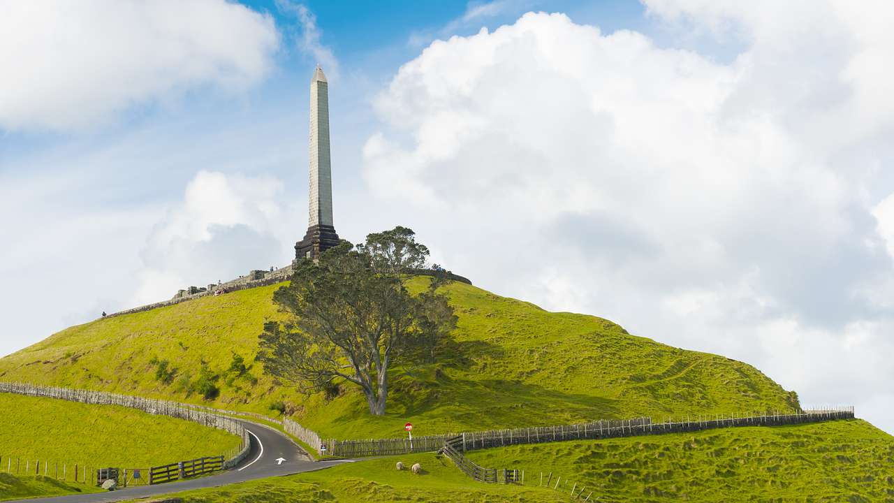 A hill full of greenery with roads, a tree, and an obelisk on top on a nice day