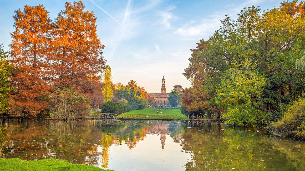 A lake surrounded by green trees in autumn shades and a tower in the distance