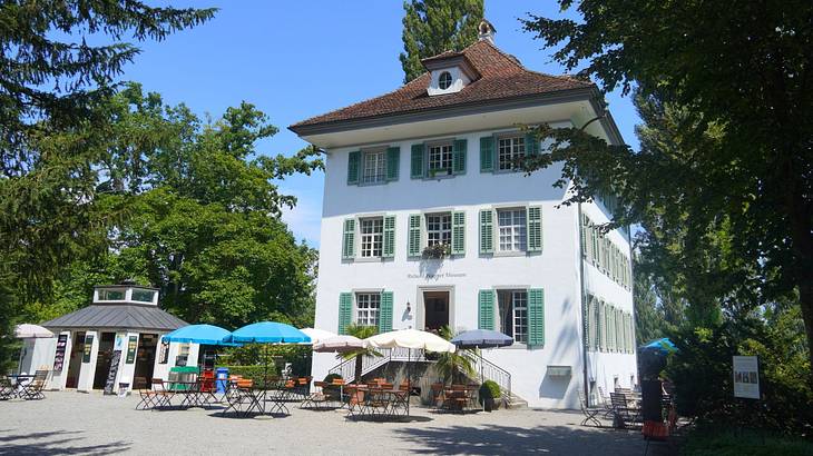 A white house with patio furniture in front surrounded by green trees