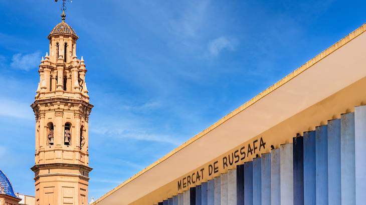Facade of a building with a sign saying "Mercat de Russafa" next to a bell tower