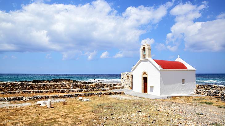 A small white church with a red roof next to the sea