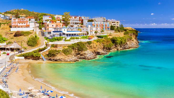 A beach next to a hill with colorful buildings under a clear blue sky