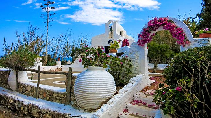 A white archway with flowers leading to an open area and a church