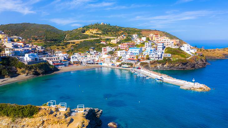 An aerial shot of a coastal village with colorful buildings on a green hill