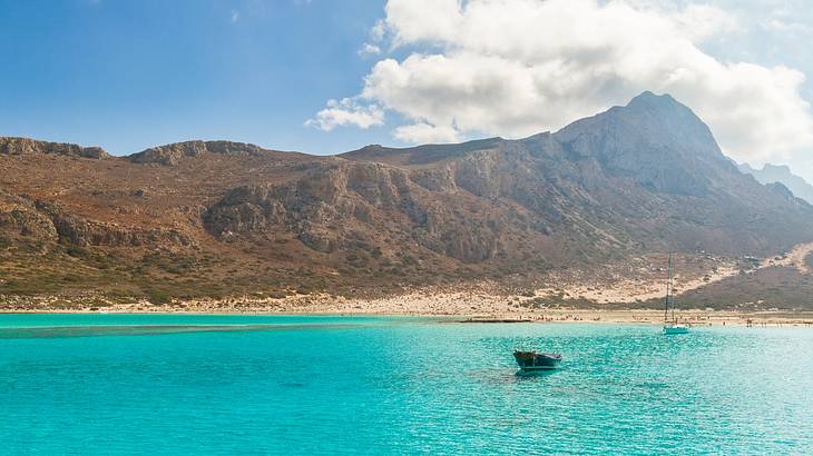 The sea with a boat on it near a mountain under a blue sky with white clouds