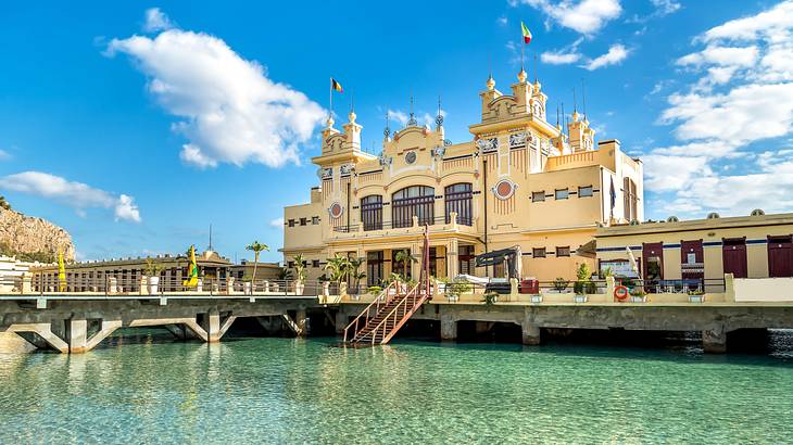 A large building with spires and flags near a bridge and a ramp to the sea