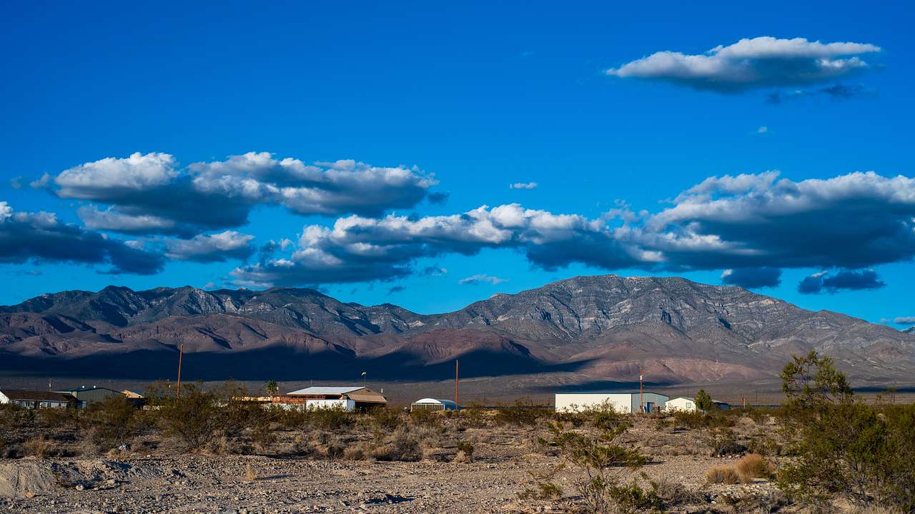 A desert near a few structures and mountains in the background on a cloudy day