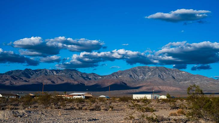 A desert near a few structures and mountains in the background on a cloudy day