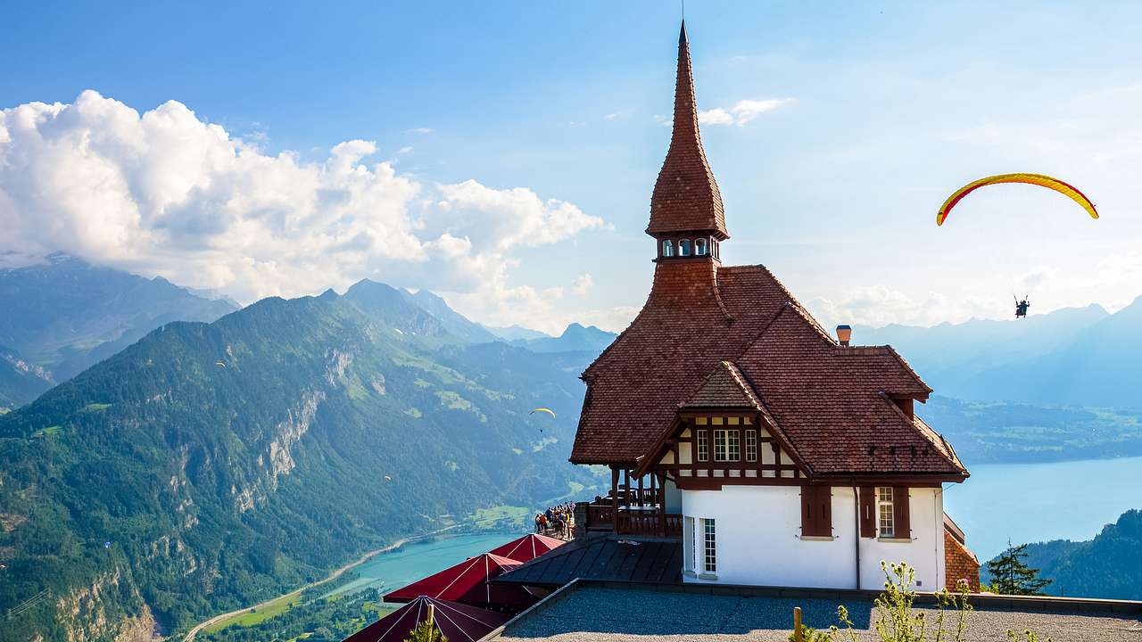 A house with a spire above water and mountains and a paraglider in the air