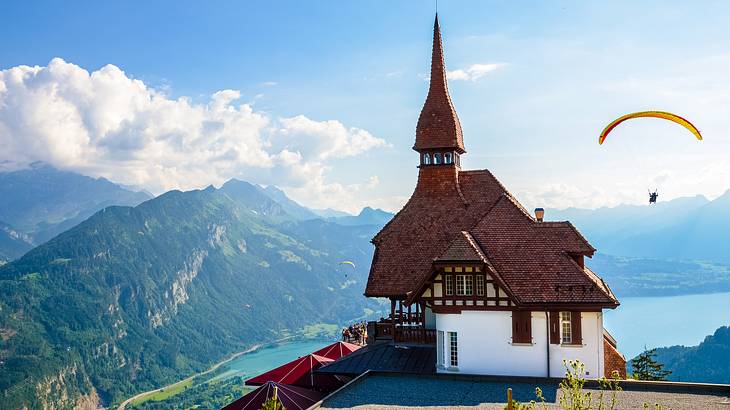 A house with a spire above water and mountains and a paraglider in the air