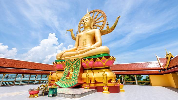 A low-angle shot of a gold sculpture of a Buddha with a colorful base