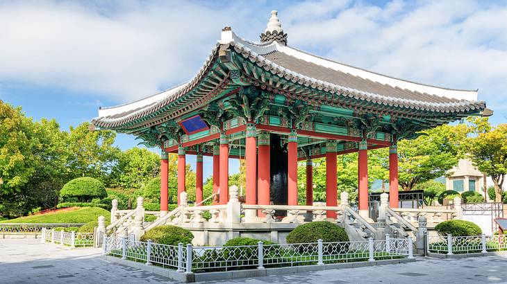 A colorful gazebo with a curved roof with tiles near trees and bushes