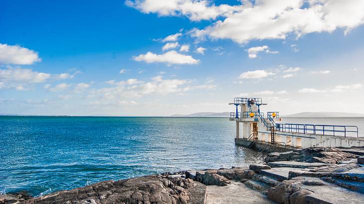 A rocky coastline with a walkway leading to a white structure